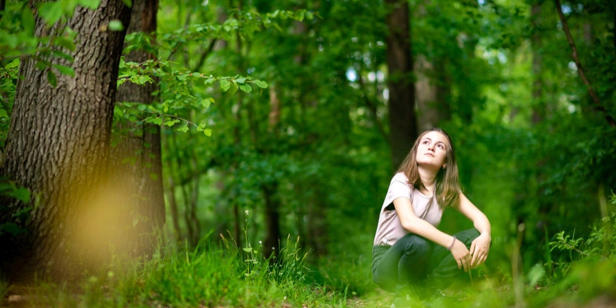 A girl looking up in a lush green forest