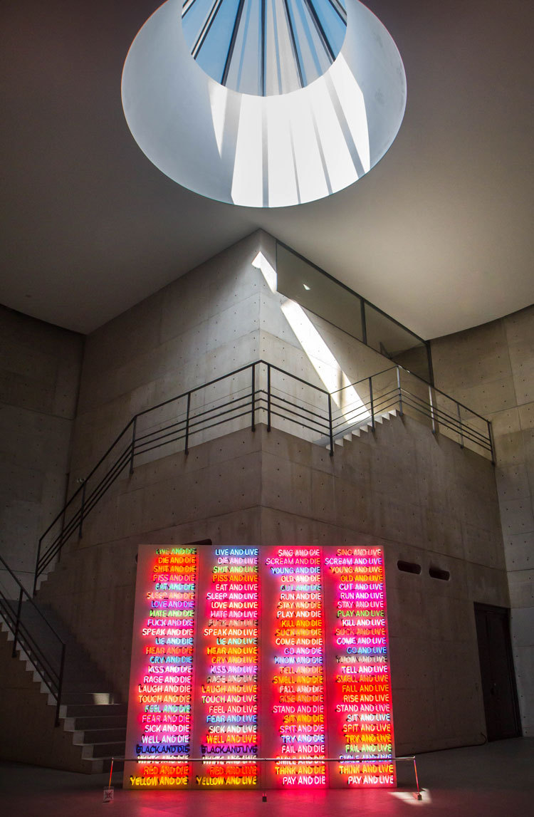 Bright pink light artwork in gallery with sun shining down through the roof.