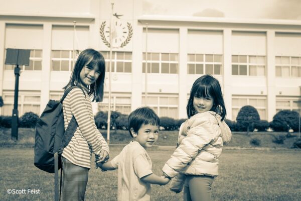 Three children holding hands outside the former school building that houses Akita Inaka School