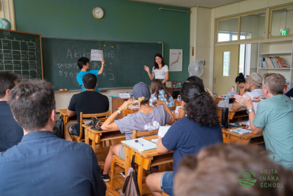 Students at wooden desks in an Akita Inaka School classroom watching a teacher at the blackboard