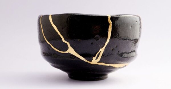 Black raku tea bowl repaired using the kintsugi crack method, with gold lacquer filling every break