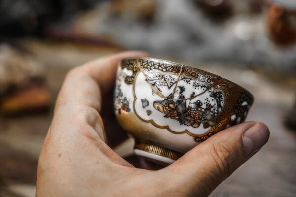 Hand holding a small ceramic bowl repaired with gold kintsugi lacquer along its cracks