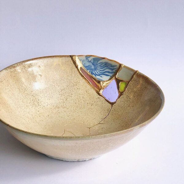 Cream glazed bowl repaired using the kintsugi joint method, with a patterned ceramic fragment set into the rim