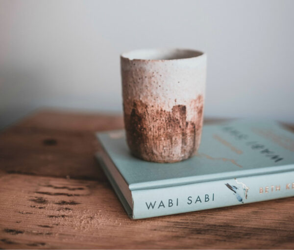 Rough glazed ceramic cup resting on a book titled Wabi Sabi on a wooden table