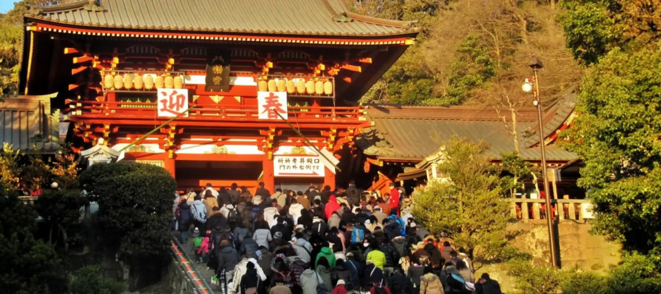 Crowds ascending the steps to a shrine during Hatsumode, the first shrine visit of the New Year, beneath a red gate adorned with festive decorations