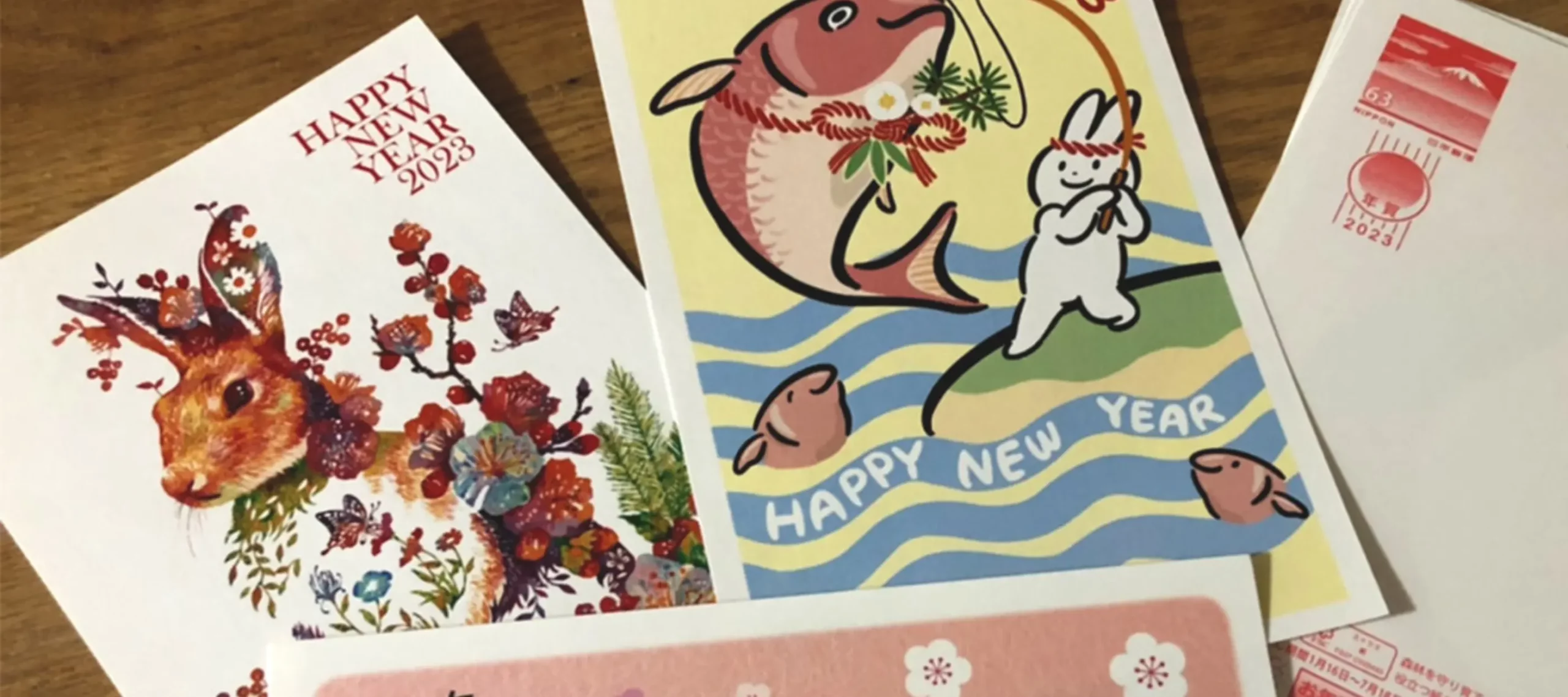 Assorted Japanese nengajō (New Year’s cards) featuring colourful illustrations, including zodiac animals, alongside a stamped envelope on a wooden surface