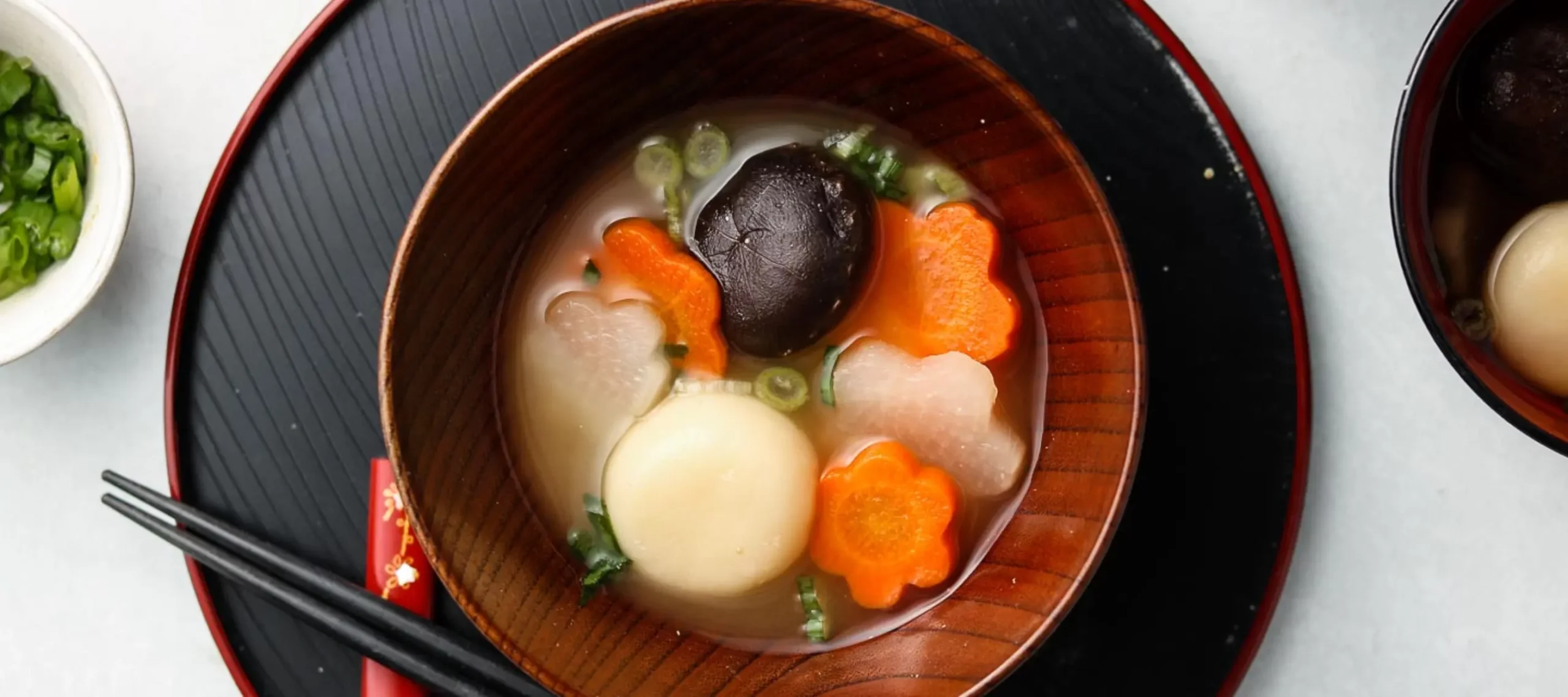 Bowl of ozoni soup with mochi, shiitake mushroom, carrot slices, and seasonal vegetables in a light broth, served in a lacquer bowl