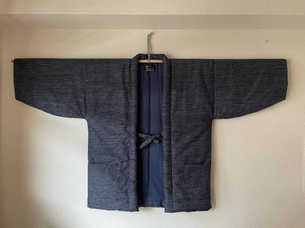 This Unisex Hanten jacket is a traditional Northern Japanese winter garment worn indoors during cold weather and heavy snowfall.
	Popularised in the 18th century, Hanten jackets were traditionally padded with a layer of cotton.
	Length: 80cm, Chest (Measured from Armpit): 63cm, Sleeve Length: 35cm
	The outer cotton layer is constructed using traditional Kurume textiles from the Chikugo region of Japan.
	The lining is a bespoke mix of cotton and polyester, formulated for optimum warmth and breathability.