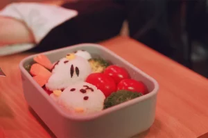 Japanese kyaraben character bento lunch box with cute rice ball faces vegetables and cherry tomatoes showing kawaii food presentation in Japanese lunch culture.