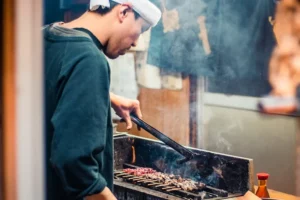 japanese street food chef grilling yakitori skewers over charcoal representing traditional shoku bunka japanese food culture and cuisine.