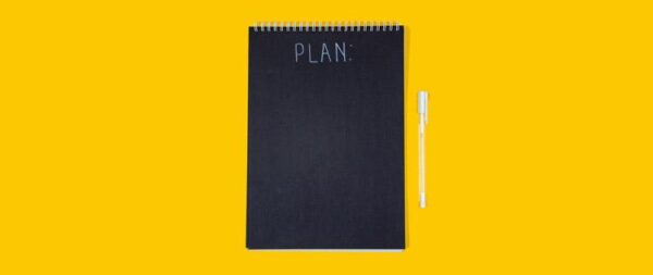 Black notepad with the word Plan and a white pen on a yellow background