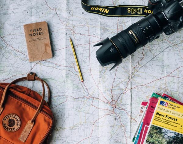 Paper map laid out with a notebook, camera, pencil and small backpack for trip planning
