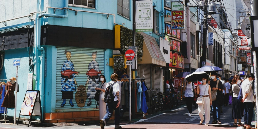 A group of people walking down a street next to tall buildings in Shimokitazawa
