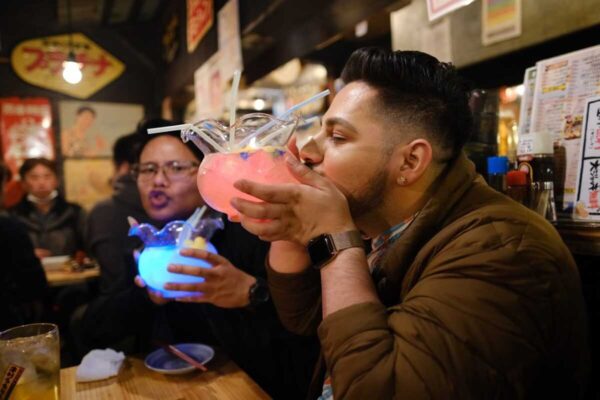 Two guests sipping glowing pink and blue fishbowl cocktails at a Tokyo izakaya
