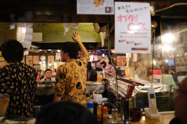Guests at the counter of a small Tokyo izakaya with handwritten menus on the wall