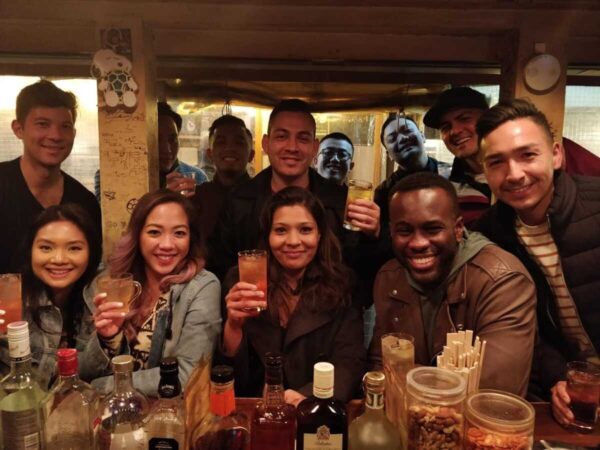 Group of guests smiling and raising drinks around a bar table on an Okawari Travels night out in Tokyo