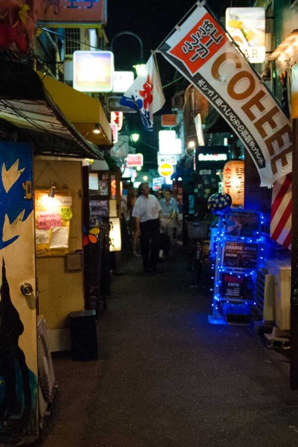 Narrow Tokyo bar alley at night lined with small bars, lanterns and a large coffee sign