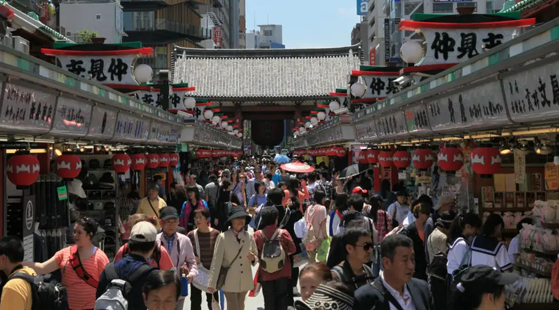 Crowds of people go through Nakamise-dori Street with a temple in the background