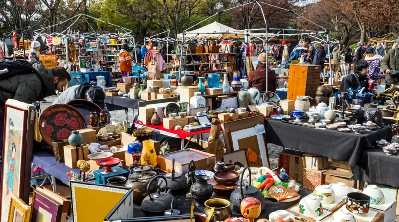 Tables filled with antiques for sale are sprawled over open grounds during daylight