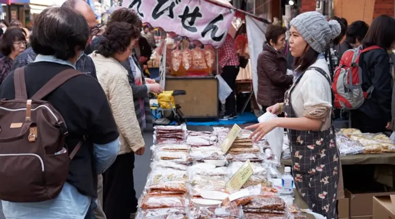 A female vendor is talking to a few interested customers over her products laid on the table