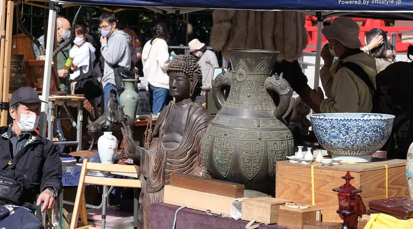 An outdoor antique market is selling various antique goods like sculptures, vases, and bowls