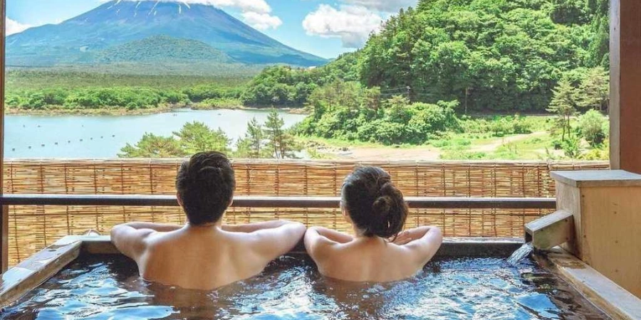 A man and a woman enjoying an onsen bath across Mount Fuji