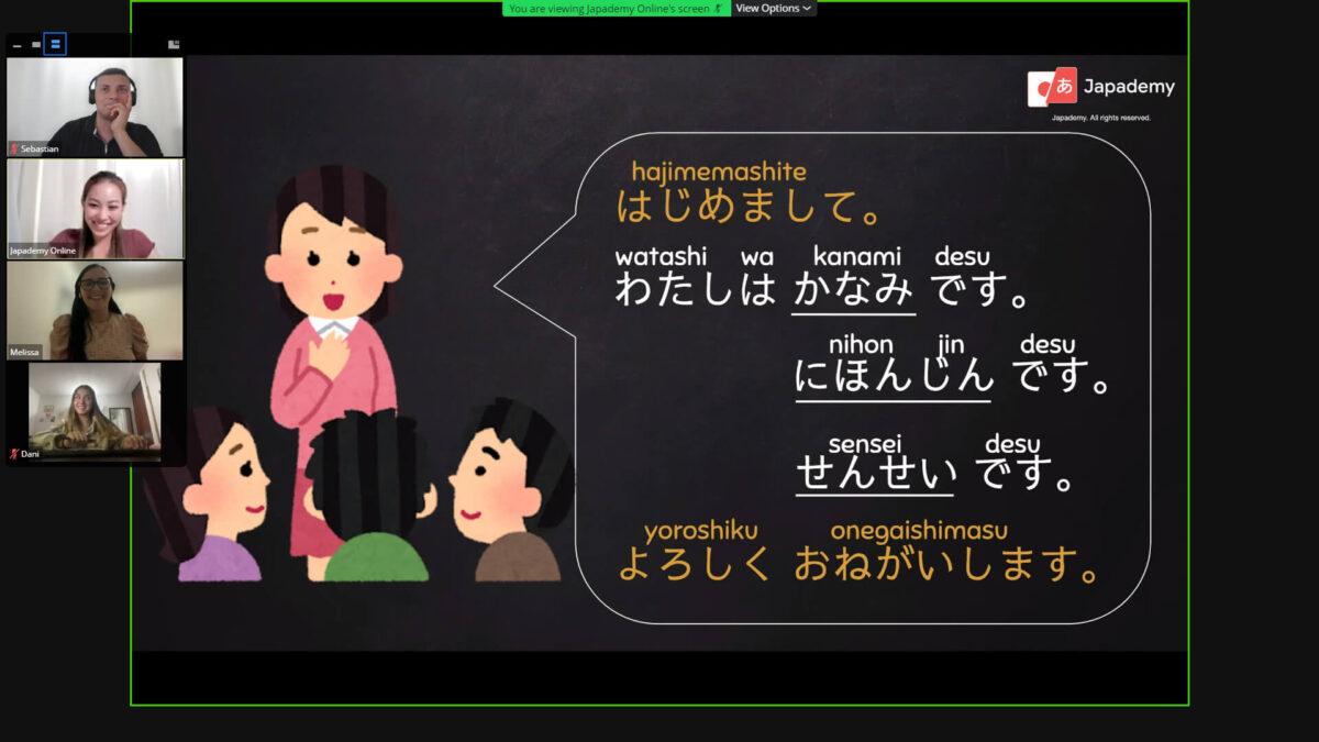 Japademy_2 Japademy online Japanese language class with students participating in a virtual lesson. The image shows a Japanese teacher illustration introducing basic phrases in Japanese, accompanied by the text 'Hajimemashite,' 'Watashi wa Kanami desu,' and other introductory phrases written in both Japanese characters and Romanized script.