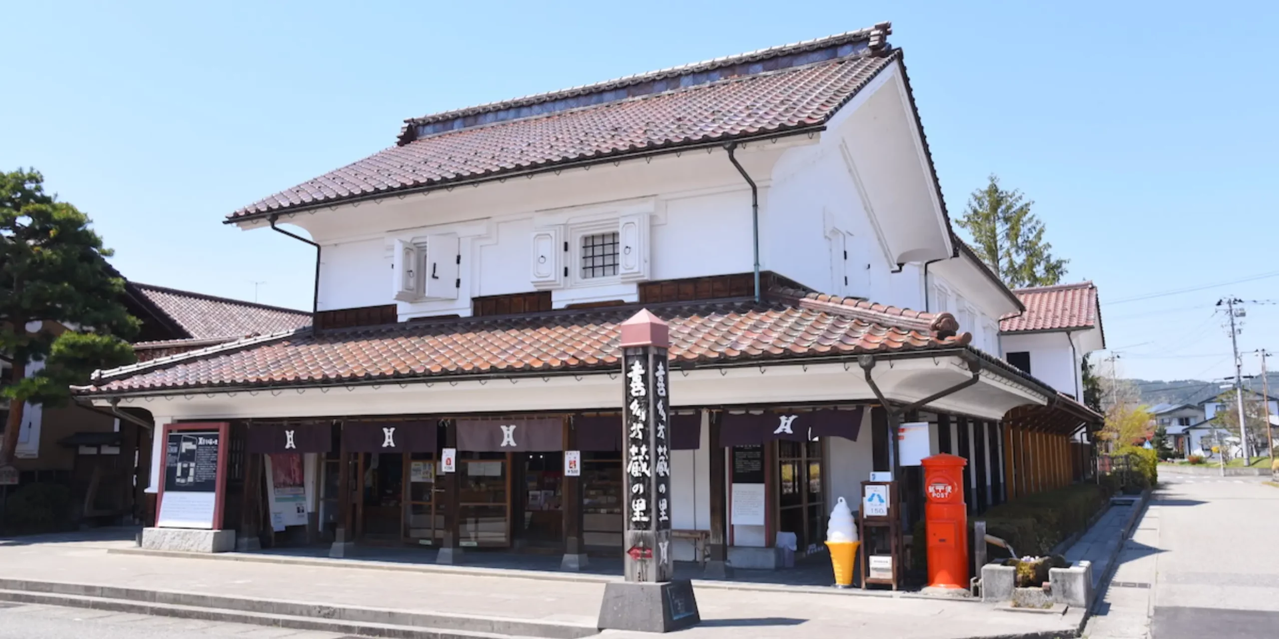 A white-walled traditional kura storehouse building on a street in Kitakata
