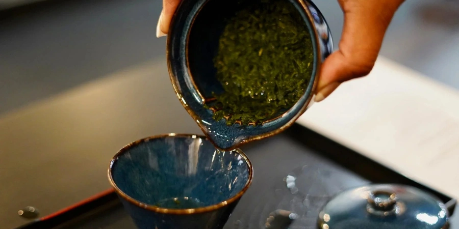 pouring steeped green tea from a filter into a ceramic tea cup