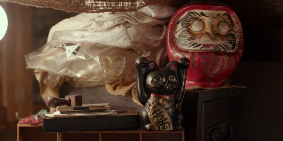 Maneki-neko and daruma doll sit on top of some boxes.