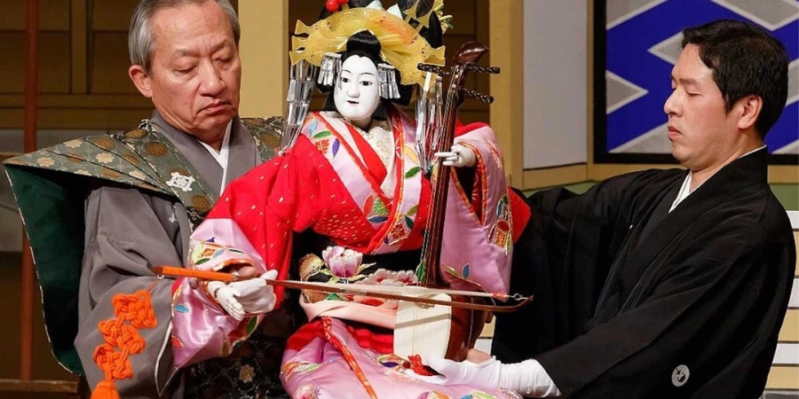 Men in black hold a set of traditional Japanese puppets