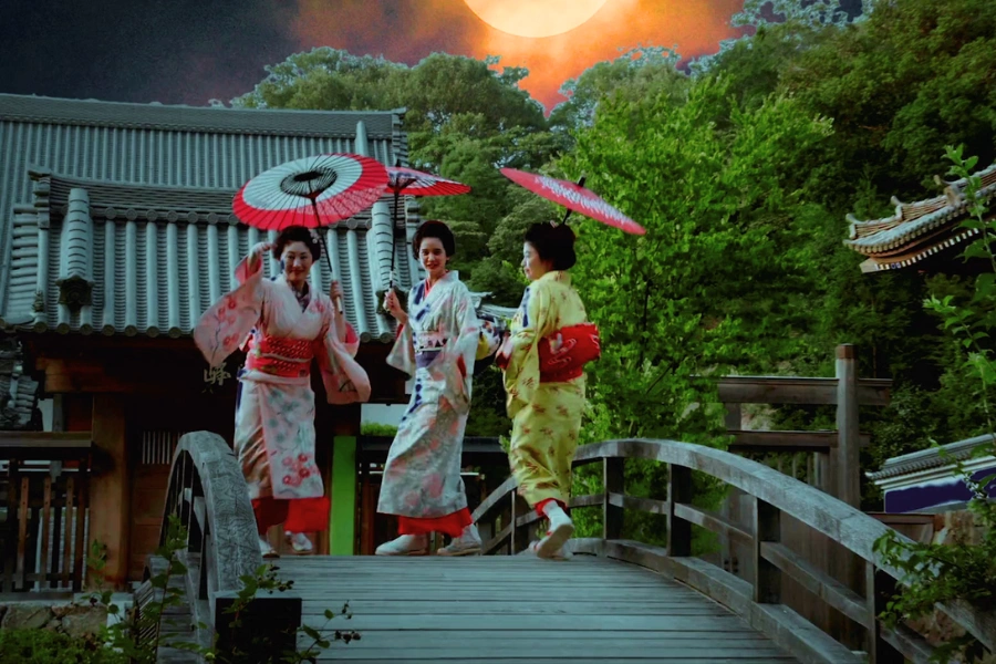 three geishas dressed in stunning red and floral-patterned kimono, walking through a historic bridge in Gion.