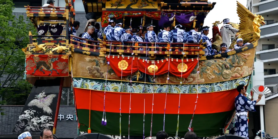 Japanese men in traditional kimonos ride a parade float that resembles an ancient Japanese boat