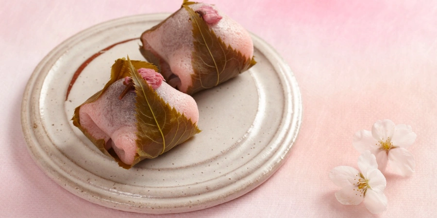 Sakura Mochi is a chewy, light pink glutinous rice ball filled with sweet red bean paste and wrapped in an edible pickled cherry blossom leaf.