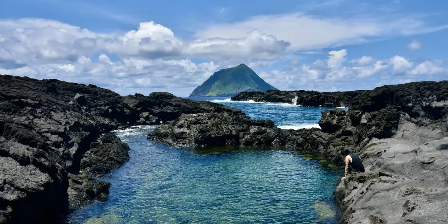 Tourist sitting on volcanic rocks on the shoreline of Hachijojima
