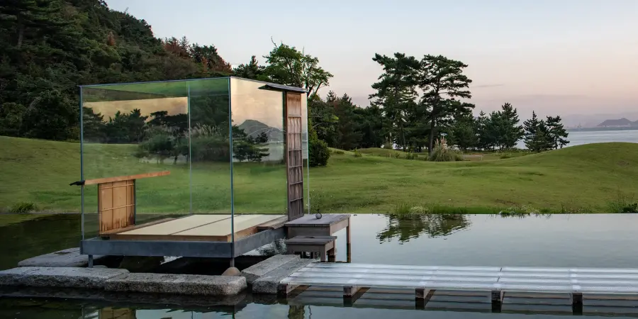 Walkway leading up to cube-shaped glass room overlooking the forest and ocean