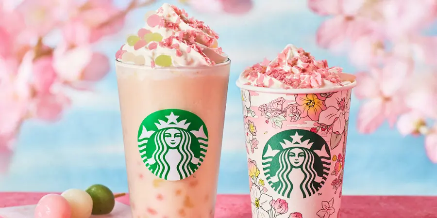 Two Starbucks drinks are shown in the picture. These drinks are sakura-themed, as their ingredients are made out of cherry blossoms. A dango is placed behind them. Cherry blossom petals surround the corners of the image.