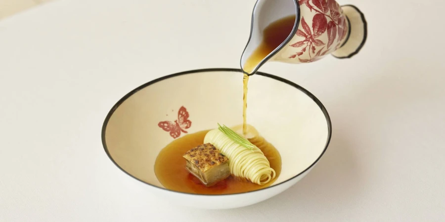 Broth being poured onto a dish on a butterfly-printed bowl