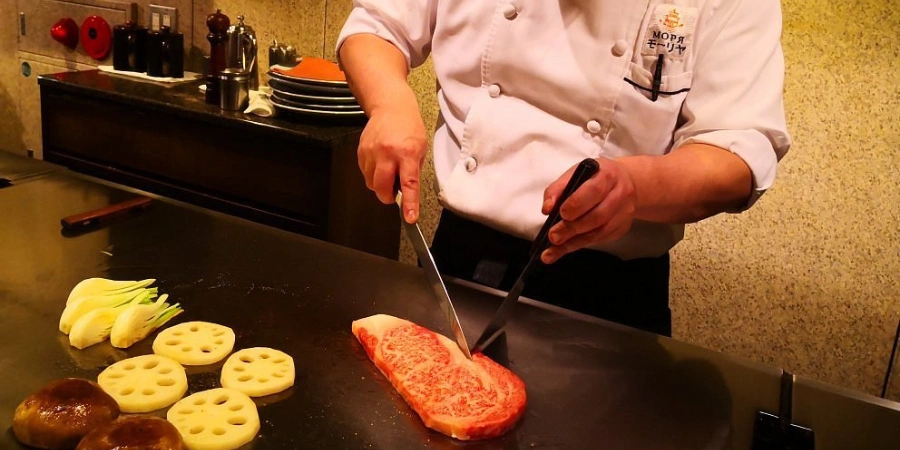 A chef cooking Japanese beef steak with some vegetables on a grill