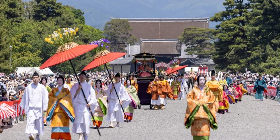 Participants in Heian-era costumes walking in the Aoi Matsuri procession in Kyoto, featuring traditional robes, parasols, and imperial Japanese cultural festival parade.