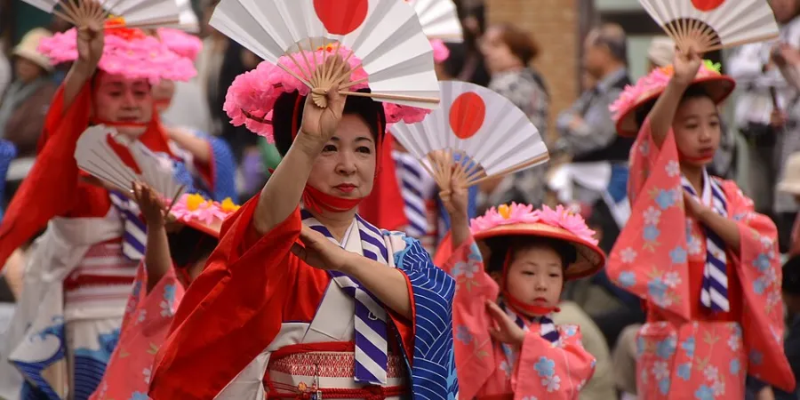 Performers in colorful kimono dancing with fans during Hakata Dontaku Festival in Fukuoka, lively Japanese street festival with cultural performances and crowds.