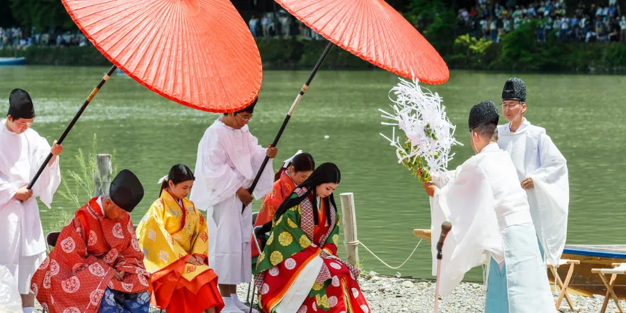 Participants in traditional Heian-era attire performing a ceremony by the river during Mifune Matsuri in Kyoto, featuring parasols and classical Japanese rituals.