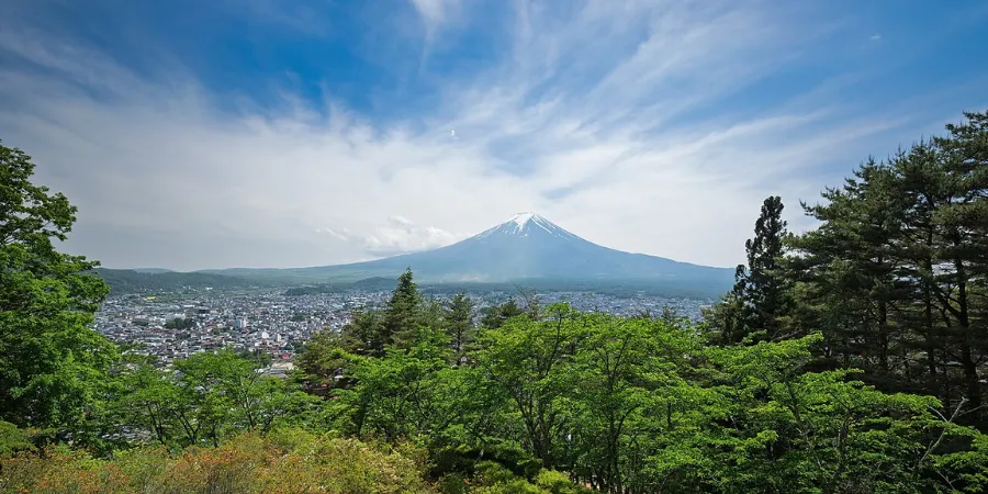 Panoramic view of Mount Fuji towering over a city and forest landscape, iconic Japanese landmark with clear skies and scenic natural surroundings.