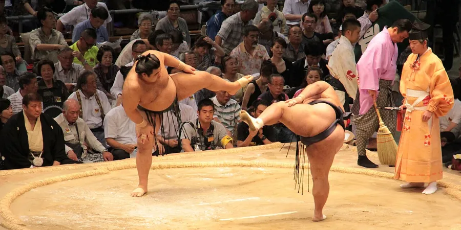 Two sumo wrestlers facing off in a traditional dohyo ring during a match in Japan, surrounded by spectators, showcasing Japanese sumo wrestling sport and cultural tradition.