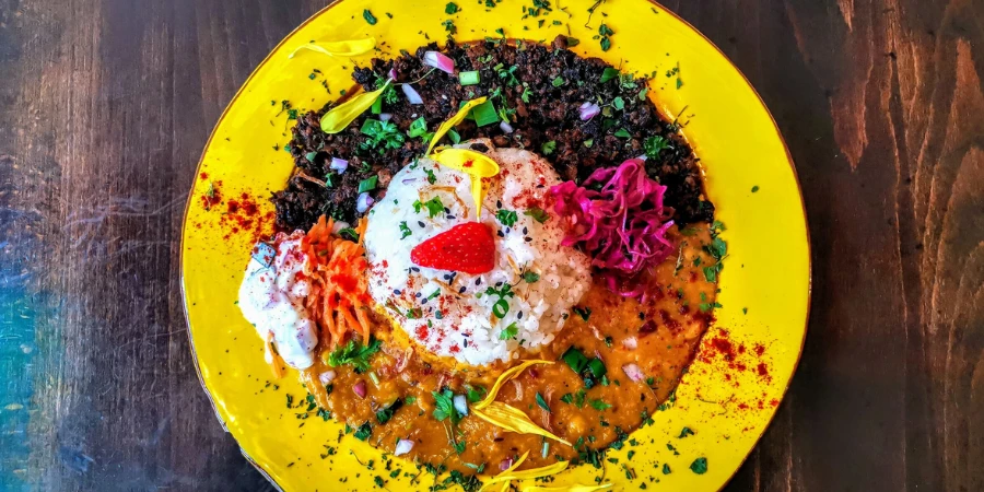 Keema and bean curry embellished with edible flowers on a yellow plate