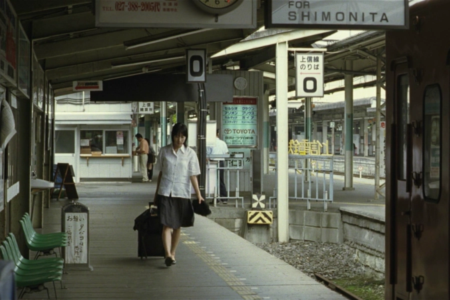 a japanese woman with a suitcase walking through the platform of a Japanese rural trainstation