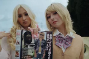 Two young women with bleached blonde hair and elaborate nail art holding an aesthetic fashion magazine representing the kogyaru substyle rebellion.