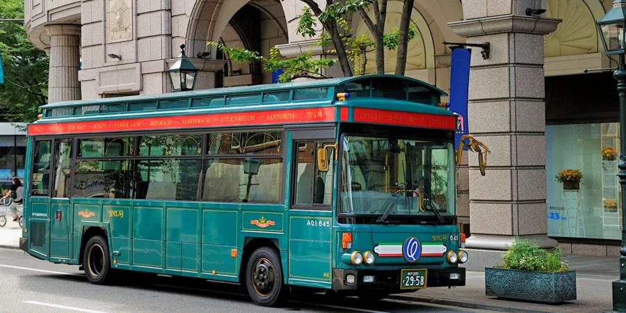 A green bus with a noticeable red strip parked on a pavement of Kobe City