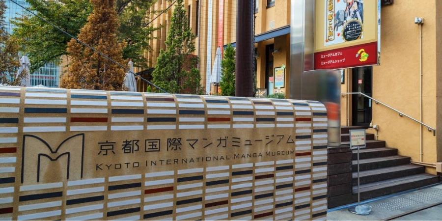 Wall signage at the Kyoto International Manga Museum displaying the name in Japanese and English, beside the entrance steps and surrounding buildings.