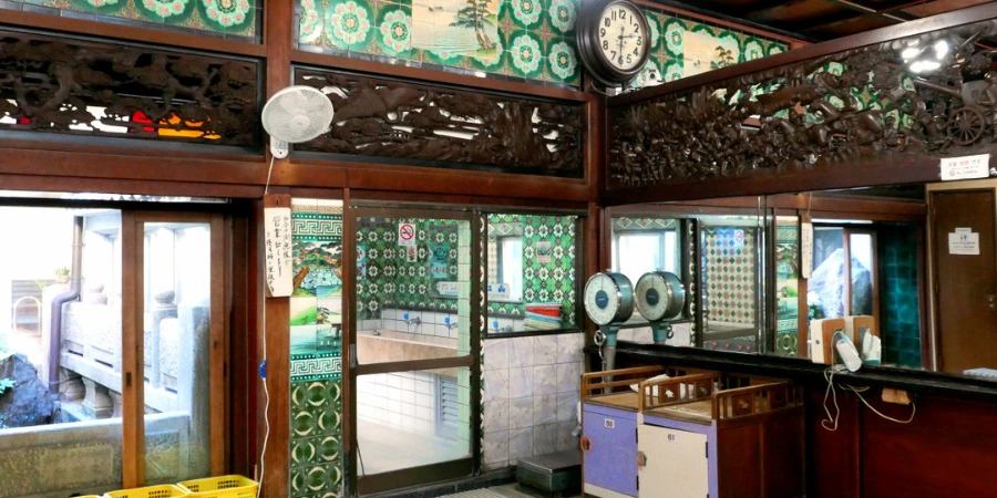 The detailed, preserved interior changing room of Funaoka Onsen, featuring intricate wood carvings, decorative green tiles, a clock, and a reflective mirror.